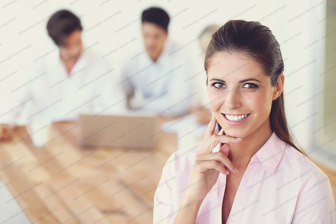 Smiling young businesswoman standing in the office with her team working in the background